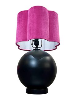 a black table lamp with a pink shade on it's side and a white background