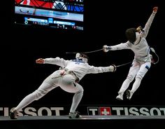 two people in white fencing suits doing tricks on a black surface with one person holding the other