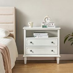 a white nightstand with books on top of it next to a bed and a plant