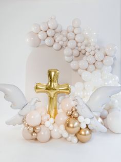 a gold cross surrounded by white balloons and other decorations in the shape of an angel