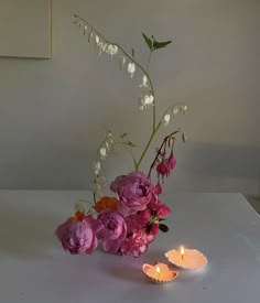 a vase filled with pink flowers next to two lit candles on a white counter top