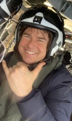 a man wearing a helmet is smiling and making the peace sign with his right hand