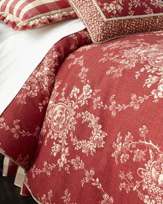 a bed with red and white comforters and pillows on top of it, next to a window