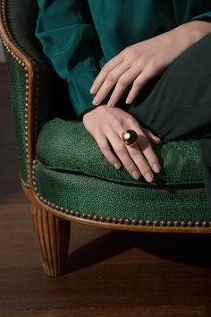 a woman's hand resting on the back of a green chair with gold ring