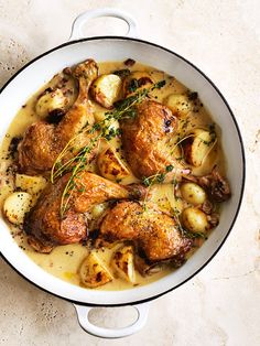 a white bowl filled with chicken and potatoes on top of a table next to a fork