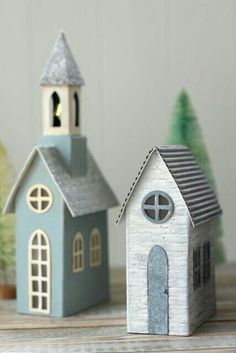 two small wooden houses sitting next to each other on top of a wood table with christmas trees in the background