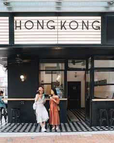 two women standing in front of a black and white building with the word hong on it