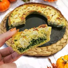 someone holding up a piece of quiche with cheese and spinach on it in front of some pumpkins