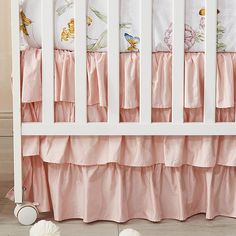 a white crib with pink ruffled bedspread and flowers on the bedding