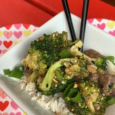 a white plate topped with rice and broccoli next to chopsticks on a table