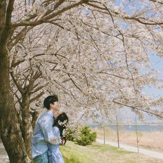 a man and woman standing next to each other under a tree with white flowers on it