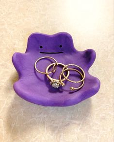 two rings are sitting on top of a purple frog shaped dish that has been placed on the floor