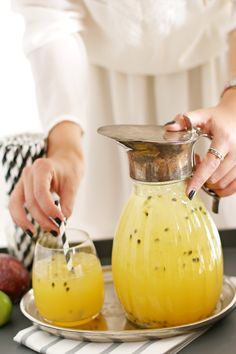 a woman is pouring orange juice into a pitcher on a tray with apples in the background