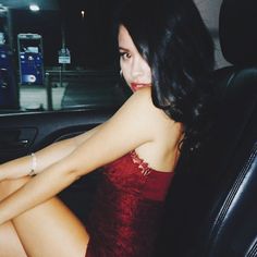 a woman in a red dress sitting in the back seat of a car with her legs crossed