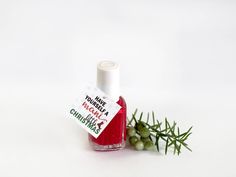 a bottle of red nail polish next to some green leaves on a white table top