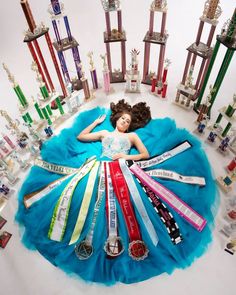 a doll laying on top of a blue blanket surrounded by trophies and ribbons in the shape of a woman's head