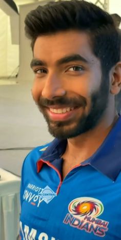 a man with a beard wearing a blue shirt smiles at the camera while standing in front of a white wall