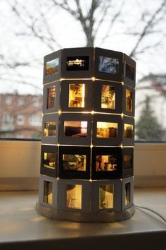 a lit up tower with pictures on it in front of a window and trees outside