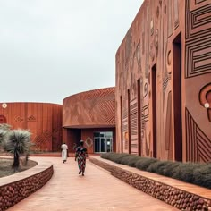 two people walking down a brick walkway in front of a building with decorative designs on it