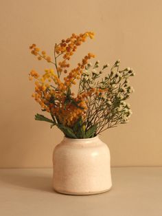 a white vase filled with yellow flowers on top of a table