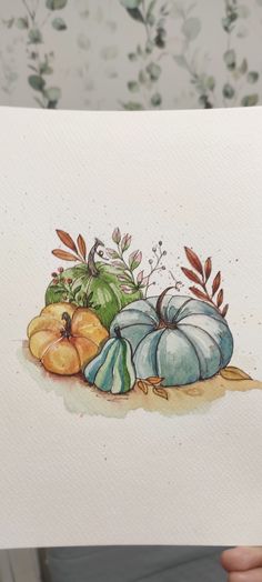 a person holding up a piece of paper with watercolor drawings of pumpkins and gourds on it