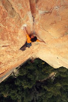 a man climbing up the side of a cliff with his hands in the air while wearing an orange jacket