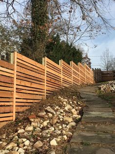 a wooden fence is lined with rocks and gravel on the side of a path next to a tree