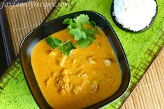 a black bowl filled with curry next to rice and cilantro on a green mat