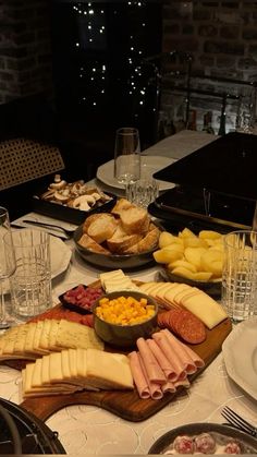 an assortment of cheeses, crackers and meats on a table with wine glasses