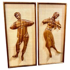 two framed wood carvings depicting people in different poses, one holding a baseball bat and the other standing up