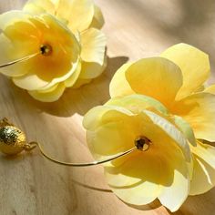 two yellow flowers sitting on top of a wooden table next to a pair of scissors