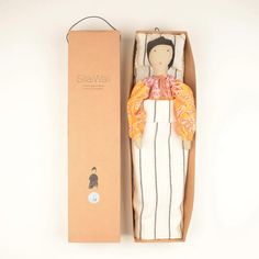 a small doll in a box next to a brown cardboard box with an orange and white design on it