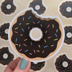 a hand holding a donut sticker with chocolate frosting and sprinkles