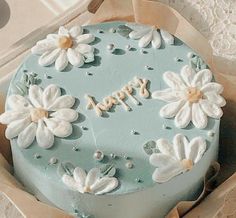 a blue cake decorated with white flowers and the words happy written on it in frosting