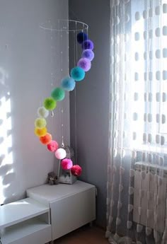 a room with a white dresser and colorful balls hanging from it's side window