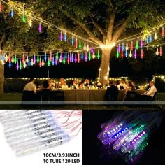 colorful lights are hanging from the tree and people sit at a table under them with candles