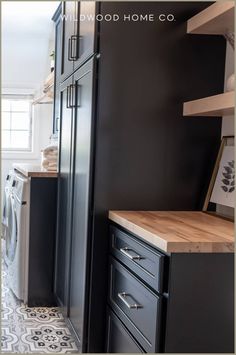 a kitchen with black cabinets and white tile flooring, along with a washer and dryer