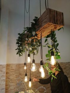 a woman is pointing at some lights hanging from the ceiling and plants growing in them