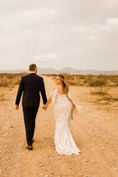 a bride and groom walking down a dirt road