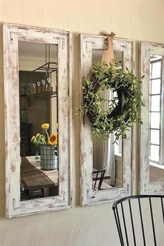 three mirrors hanging on the wall next to a chair and table with flowers in it