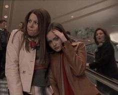 two women are standing on an escalator and one is covering her face with her hand