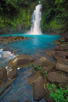 a waterfall in the middle of a river surrounded by rocks and greenery on either side