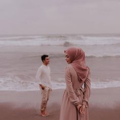 a man standing next to a woman on top of a sandy beach near the ocean