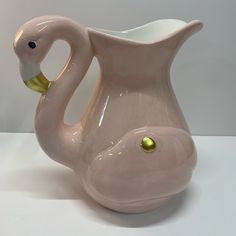 a pink ceramic swan shaped vase with gold accents on the bottom and sides, sitting on a white surface