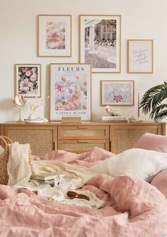 an unmade bed with pink linens and pictures on the wall