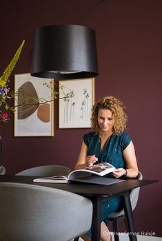 a woman sitting at a table with a book in front of her and a lamp above her