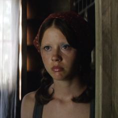 a young woman with blue eyes looking at the camera while standing in front of a door