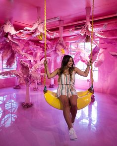 a woman sitting on a swing in a room with pink walls and palm trees behind her