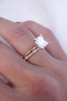 a woman's hand with a diamond ring on top of her finger and the other hand holding an engagement ring