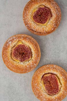 three pastries sitting on top of a table covered in powdered sugar and jelly